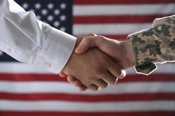 Soldier and businessman shaking hands against flag of USA