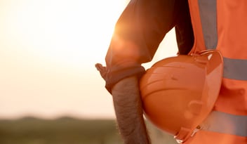Worker holding orange hard hat at sunset